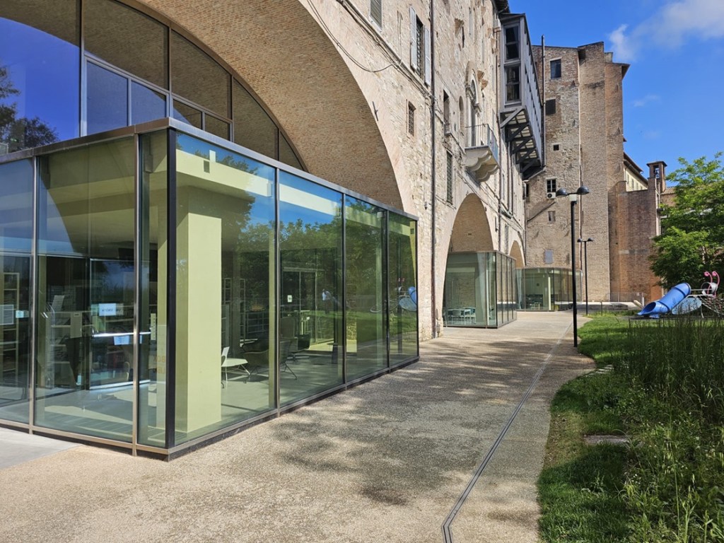 Vista della Biblioteca degli Arconi a Perugia, con strutture in vetro e architettura storica, circondata da spazi verdi.
