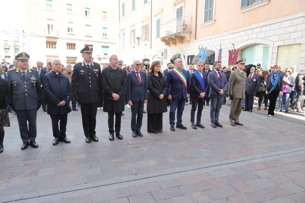 A group of officials and dignitaries standing in a row during a public event, with a crowd gathered in the background.
