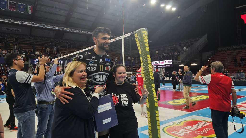 Un giocatore di pallavolo sorridente posa con due tifose in un palazzetto dopo la vittoria della Sir Susa Vim Perugia.