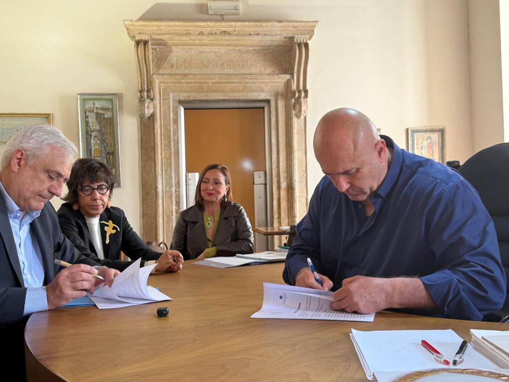 Four individuals seated at a table, engaged in signing documents in an official setting.