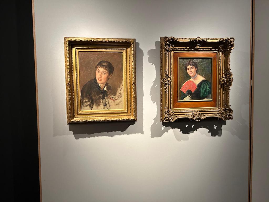 Due dipinti appesi a una parete: a sinistra un ritratto di un giovane uomo e a destra un ritratto di una donna con un ventaglio rosso.