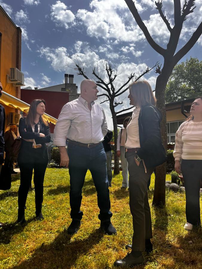 Il sindaco di Terni, Stefano Bandecchi, visita le strutture psichiatriche socio-sanitarie Tepee, Iglù e Dom, mentre discute con i presenti in un giardino soleggiato con cielo sereno e nuvole sparse.