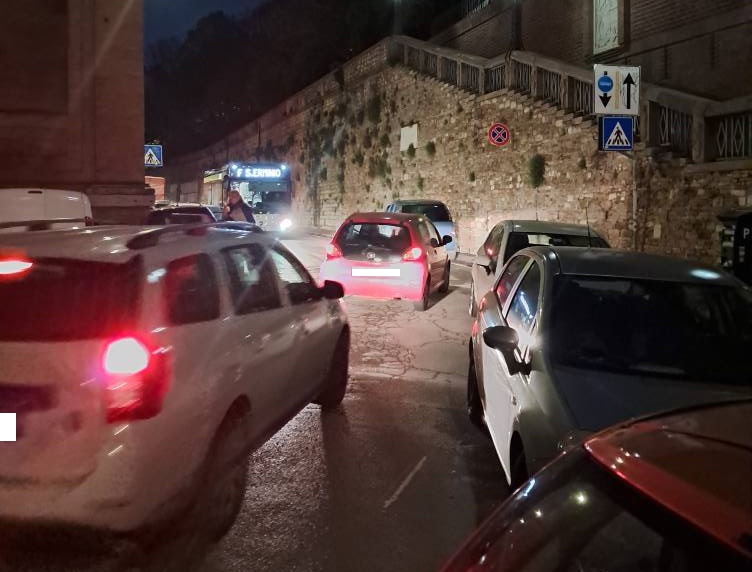 Strada trafficata di notte con diverse auto parcheggiate in modo irregolare, creando congestione nel centro di Perugia.