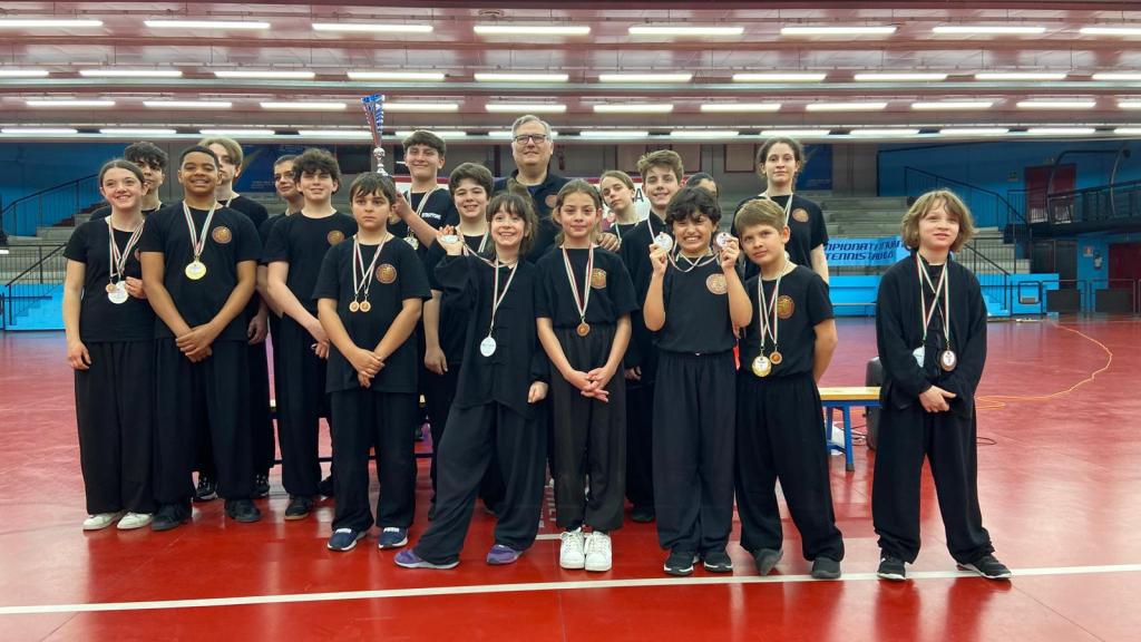 Gruppo di atleti di Wushu-Kung Fu in divisa nera, con medaglie, in piedi in un'area di competizione, celebrando un torneo.