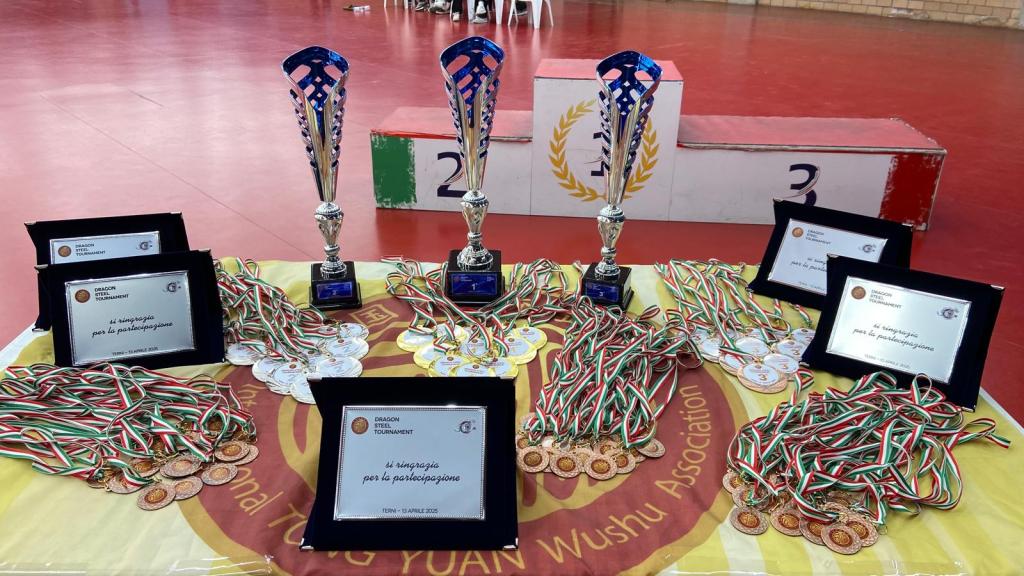 Trofei e medaglie del Dragon Steel Tournament di Wushu-Kung Fu, con premi sui tavoli e il numero 2 in evidenza sullo sfondo.