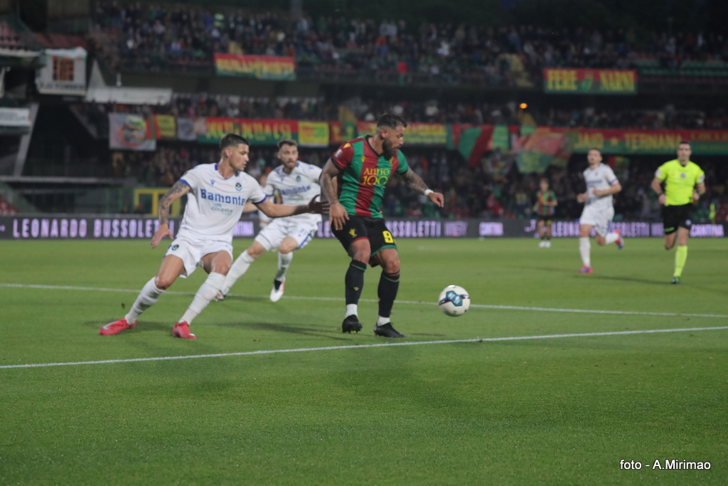 Giocatore della Ternana, in maglia verde e rossa, controlla la palla mentre un avversario della Giana Erminio tenta di bloccarlo durante una partita di calcio.