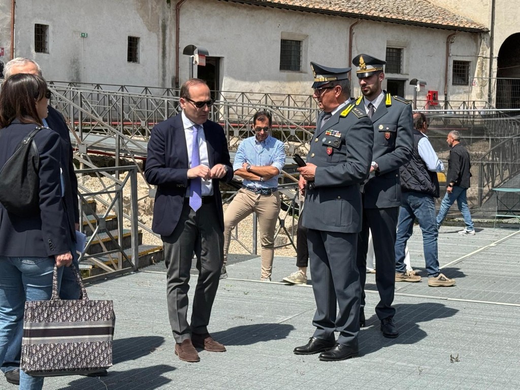 A group of individuals, including officials in uniforms, engaged in conversation outdoors near a building structure.