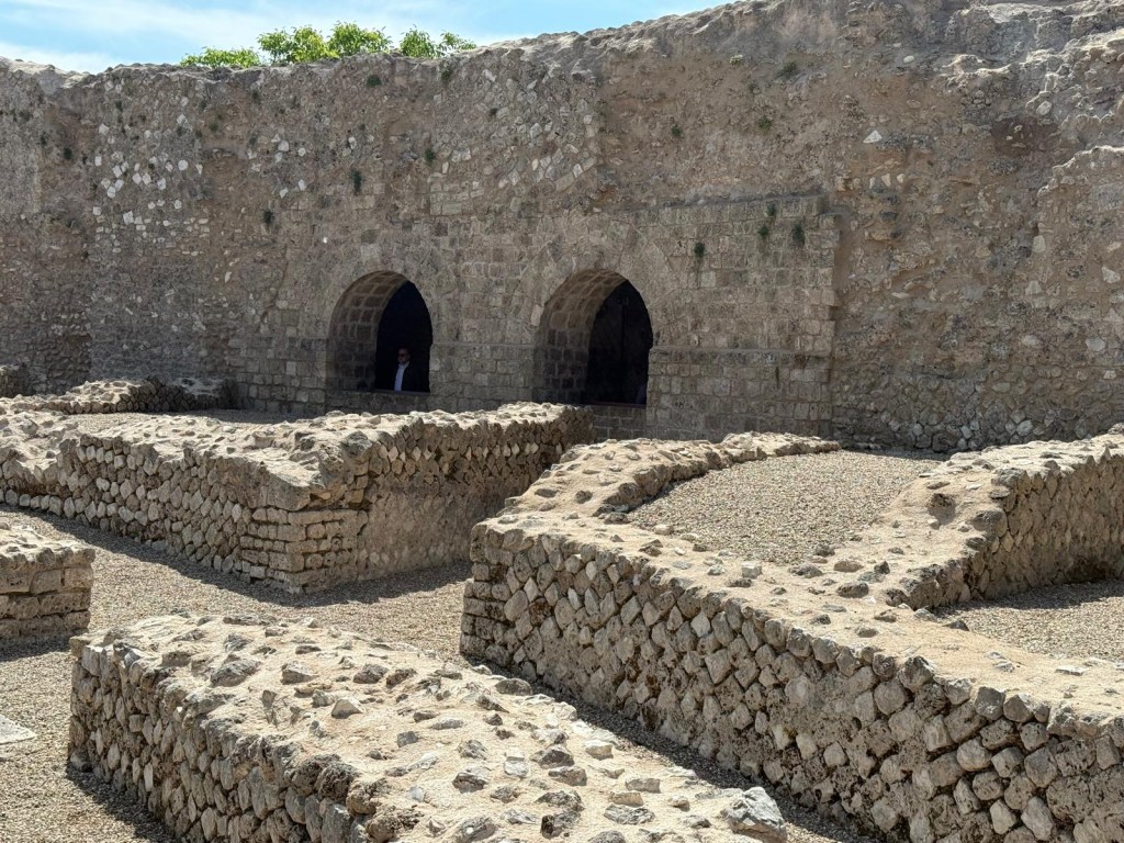 Ruins of an ancient stone structure with arched doorways and surrounding rocky terrain.