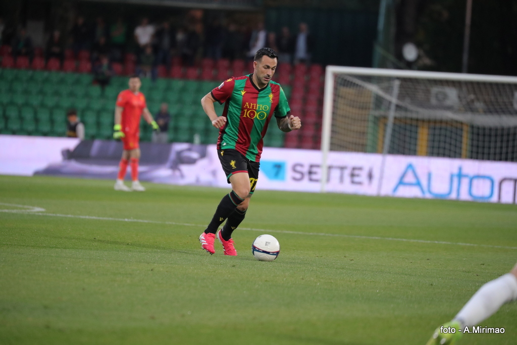 Giocatore in campo, indossando la maglia della Ternana con colori rosso e verde, mentre controlla il pallone durante una partita di calcio.