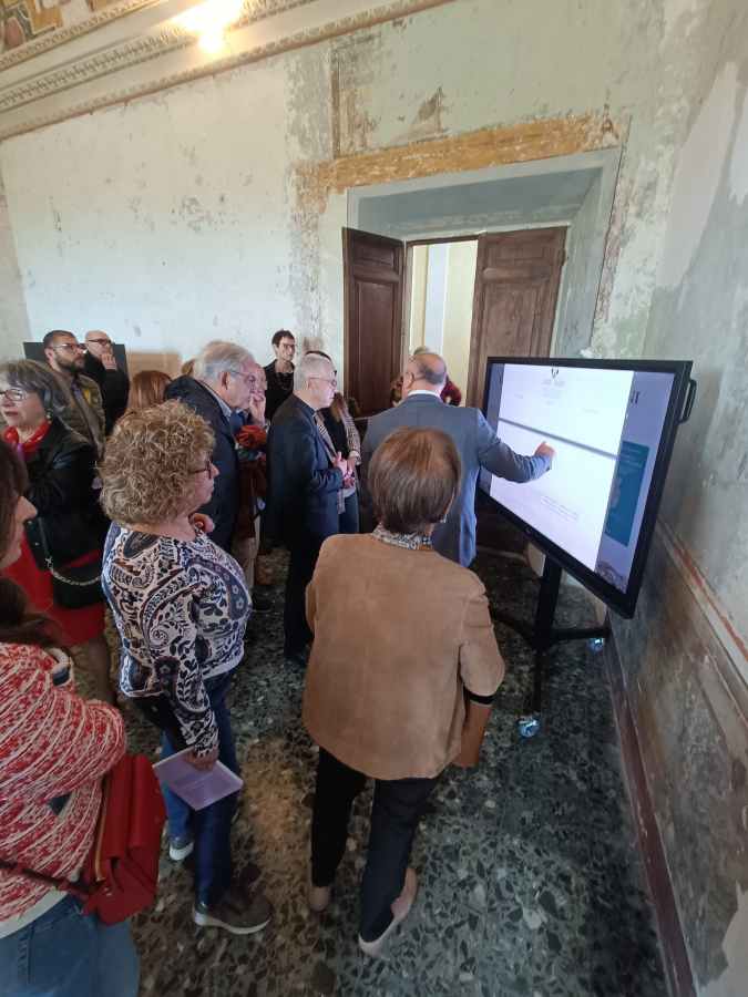 Visitori interagiscono con un'infografica multimediale durante l'inaugurazione di una mostra su Alessandro Geraldini presso Palazzo Petrignani ad Amelia.