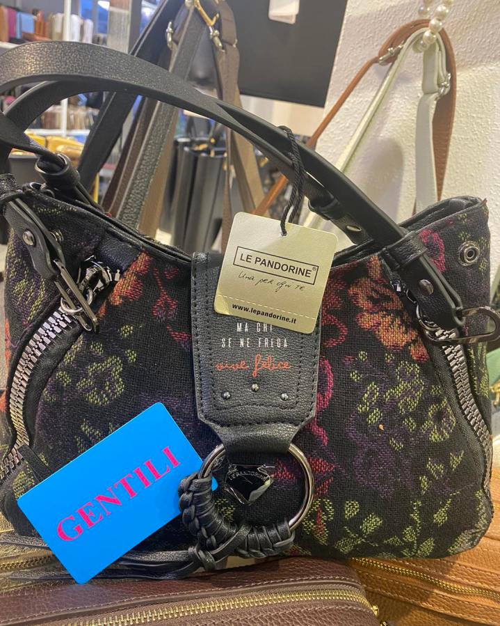 Una borsa di design in tessuto con manici neri e dettagli floreali, esposta in un ambiente di vendita accogliente.