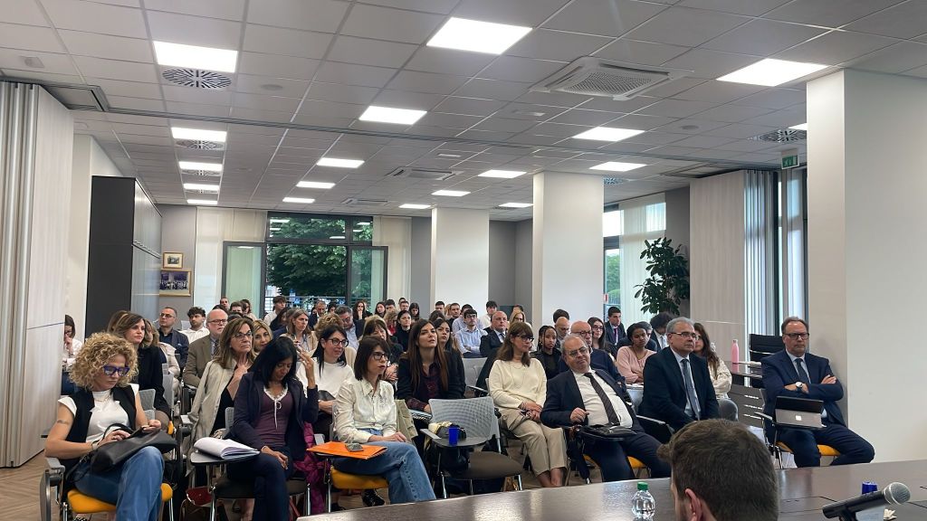 Un importante convegno giuridico con un pubblico di esperti e professionisti del settore legale si svolge in una sala moderna e ben illuminata.
