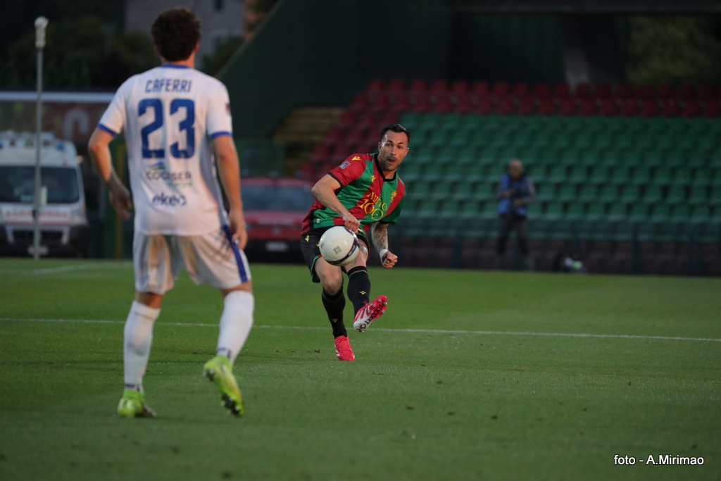 Giocatore della Ternana in azione con un pallone durante una partita contro la Giana Erminio, sullo sfondo uno stadio parzialmente occupato.