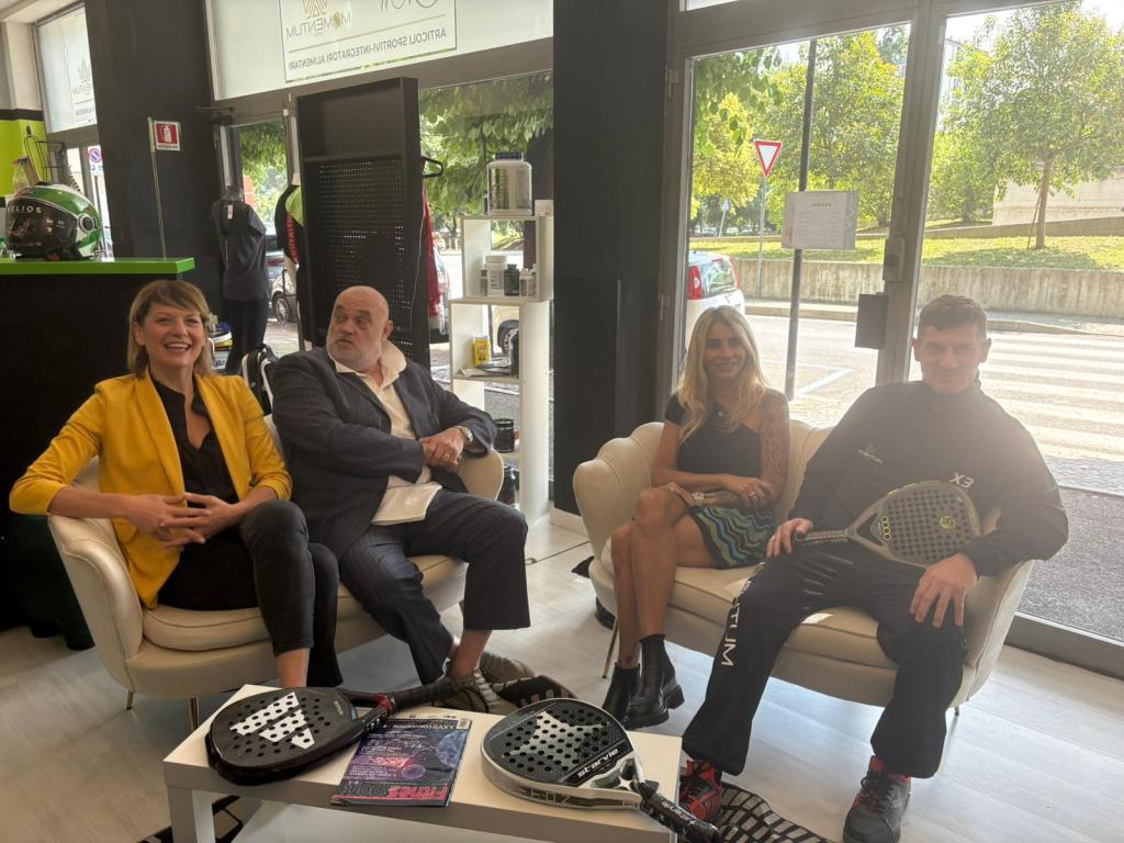 Quattro persone sedute in salotto con racchette da padel, sorridono durante un incontro informativo su lezioni di padel.