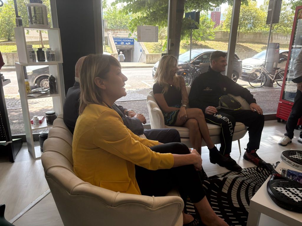 Un gruppo di persone sedute in una sala elegante durante una conferenza, con scelte di arredamento moderno e attrezzatura per il padel visibile in primo piano.