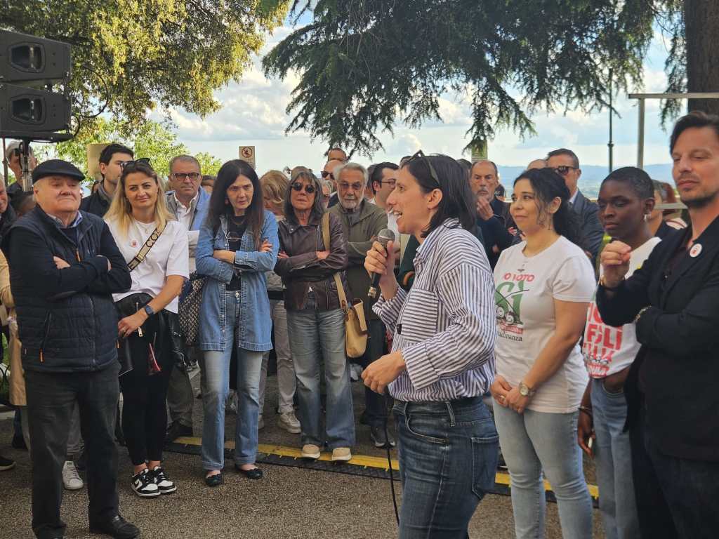 Elly Schlein, segretaria del Partito Democratico, parla a un pubblico durante un evento a Perugia, con cittadini e membri del partito presenti.