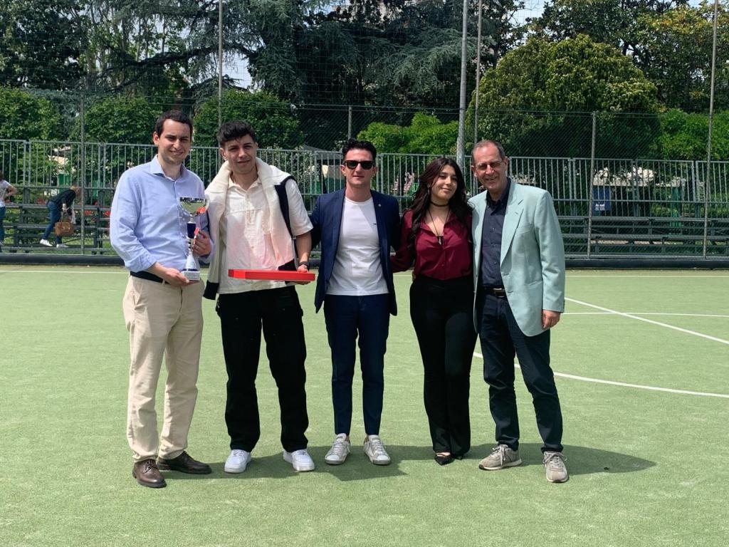 Gruppo di persone sorridenti in un campo da calcio, con un trofeo e un premio in mano, durante il torneo di beneficenza Memorial Erika Campili.