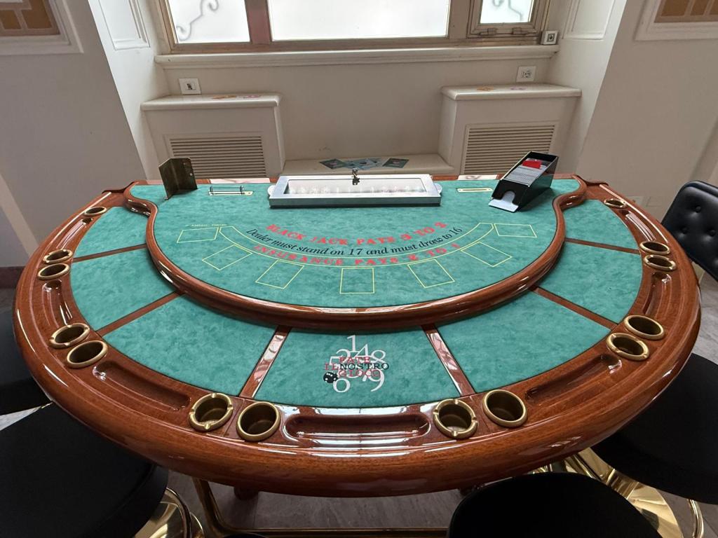 A green felt blackjack table with wooden edges, featuring card slots and a betting area, surrounded by black chairs.