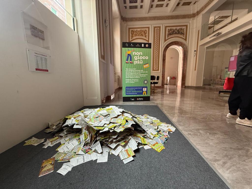 A pile of discarded lottery tickets on a carpeted floor in a building, with a sign in the background promoting responsible gaming.
