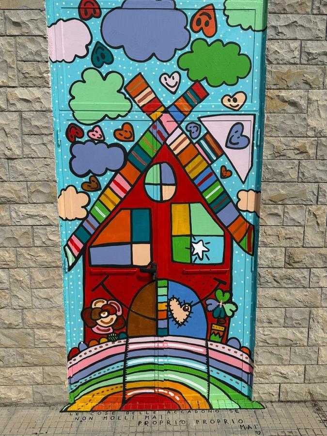 Porta della palestra decorata con colori vivaci e disegni giocosi, rappresentante una casa con un arcobaleno, nuvole e cuori.