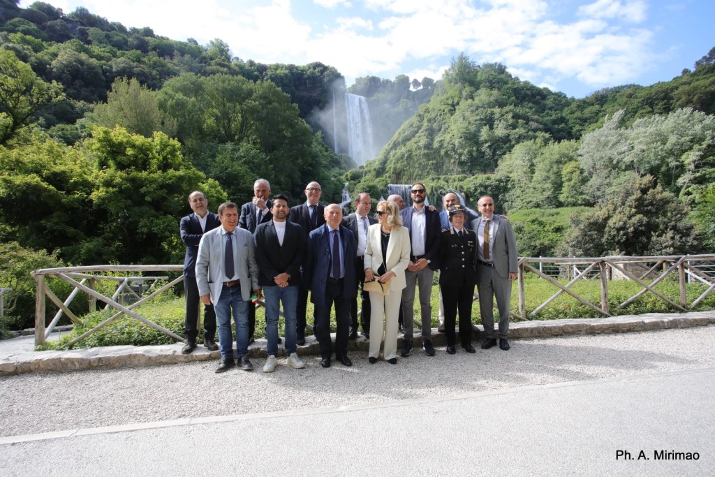 Gruppo di persone sorridenti in piedi davanti a una cascata e un paesaggio verde