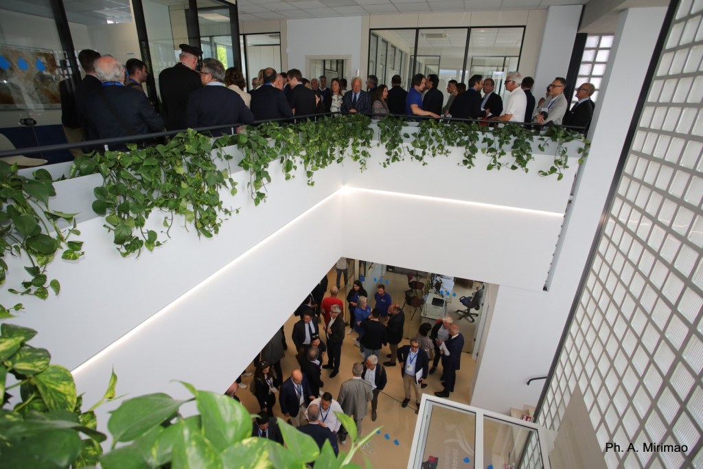 Aerial view of an event at the new headquarters of the Tevere-Nera Consortium, with attendees gathered on both floors and green plants along the balcony.