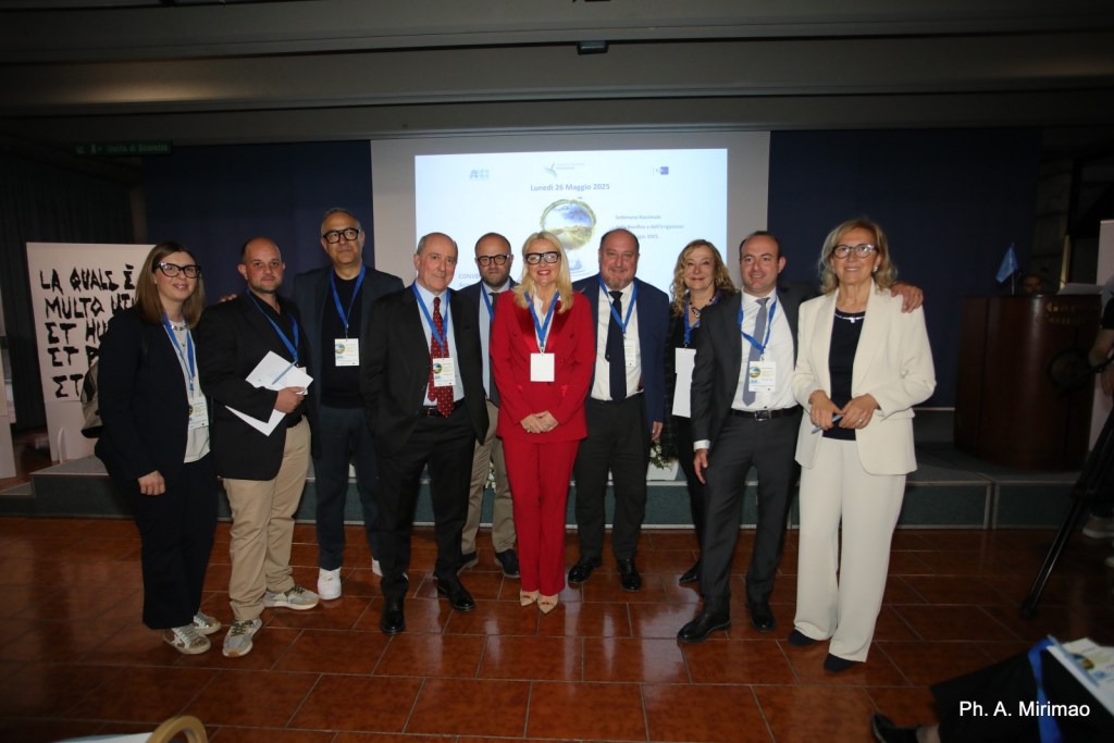 Gruppo di persone sorridenti in un evento, con sfondo di presentazione, che partecipa a un convegno al Hotel Garden di Terni.