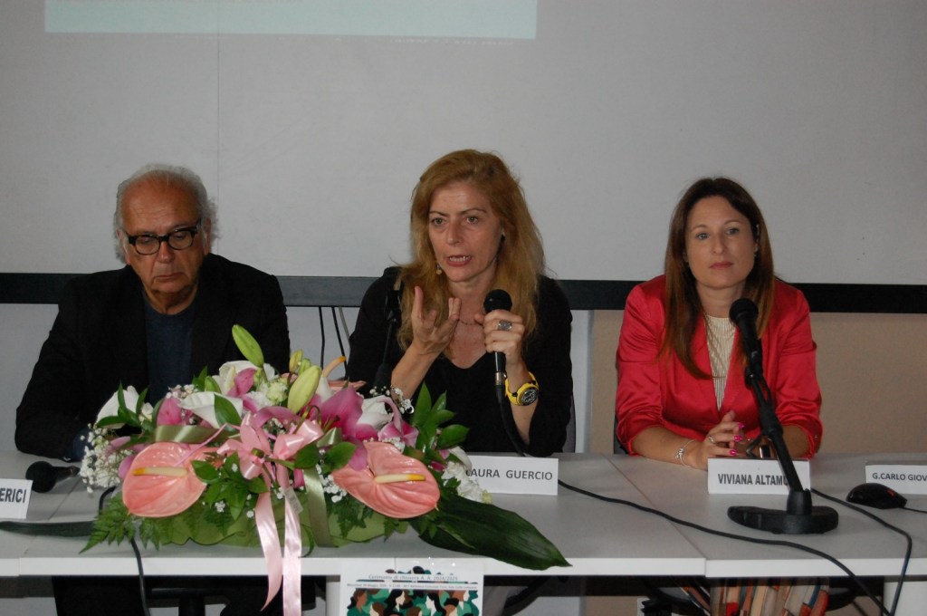 Evento di chiusura dell'anno accademico dell'Università della Terza Età di Terni, con Laura Guercio che parla al microfono, accompagnata da due relatori e un bouquet di fiori sul tavolo.