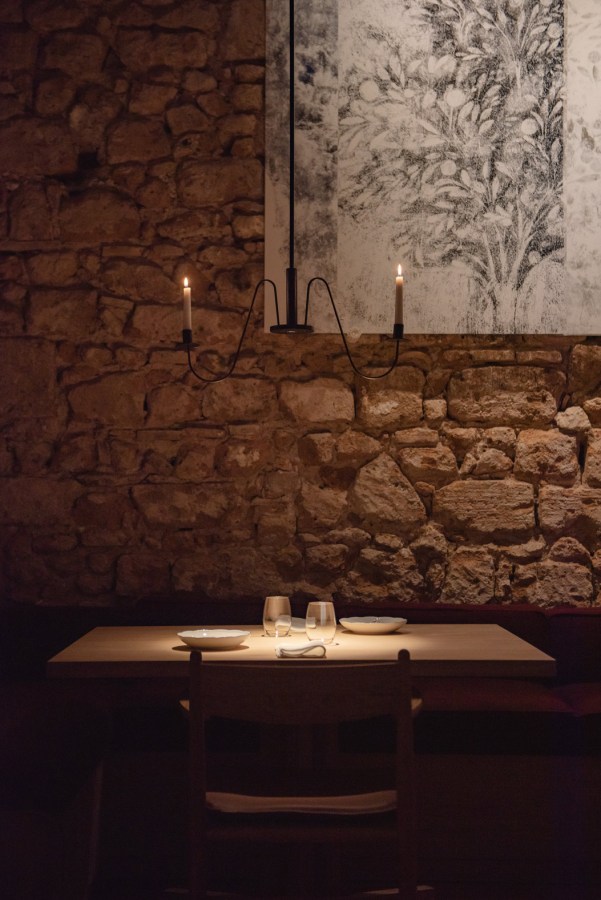 Interno del ristorante Coro di Orvieto, con un tavolo ben apparecchiato illuminato da una candela, circondato da una parete di pietra e un'opera d'arte appesa.