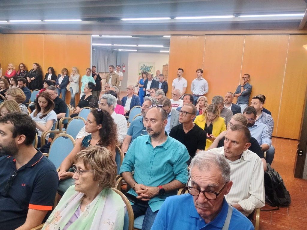 A diverse group of people seated and standing in a conference room, engaged in a discussion or presentation.