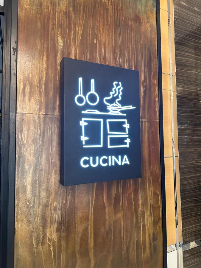 Insegna luminosa del ristorante Cucina, con elementi grafici di utensili da cucina, affissa su una parete elegante.