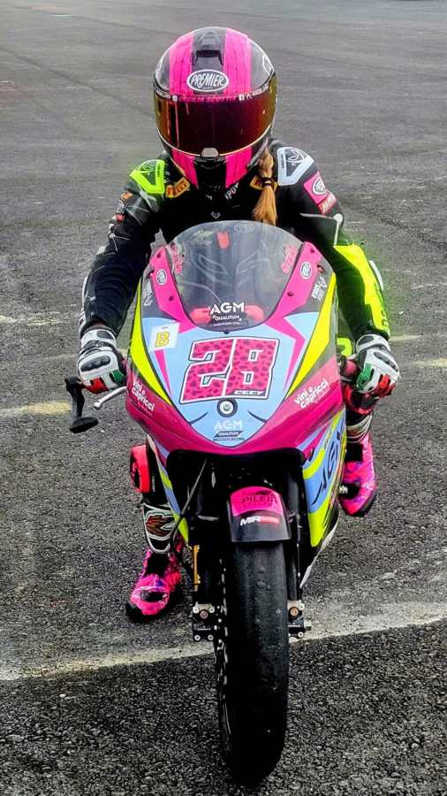 Pilota in posa su una moto da corsa colorata con tuta di sicurezza, pronta per una competizione motociclistica.