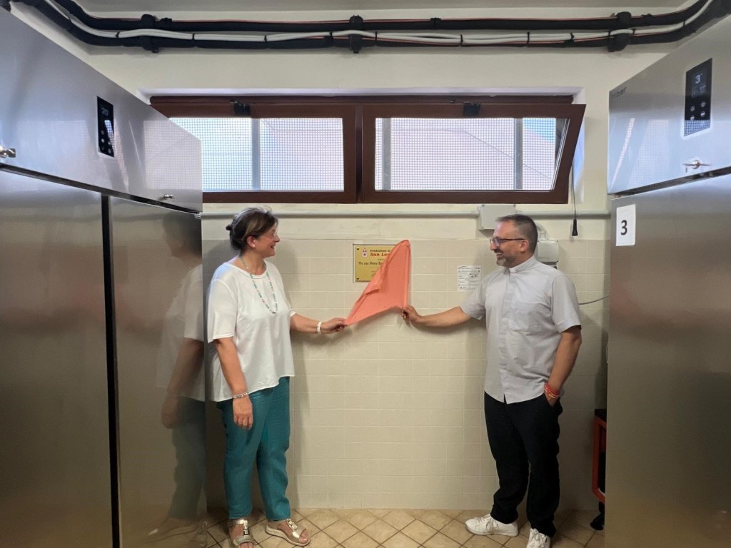 Inaugurazione di nuovi armadi refrigerati nella mensa Caritas 'Don Gualtiero', con due persone che scoprono una targa commemorativa.