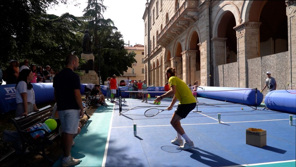 Un momento di minitennis durante il torneo a Perugia, con giocatori che praticano sul campo mentre una folla di spettatori assiste.