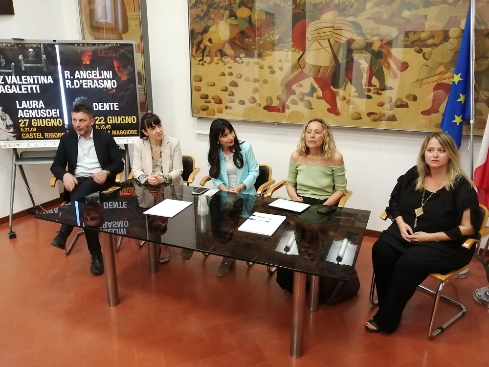 Una conferenza dedicata al festival Moon in June, con ospiti seduti attorno a un tavolo e manifesti degli artisti sullo sfondo.