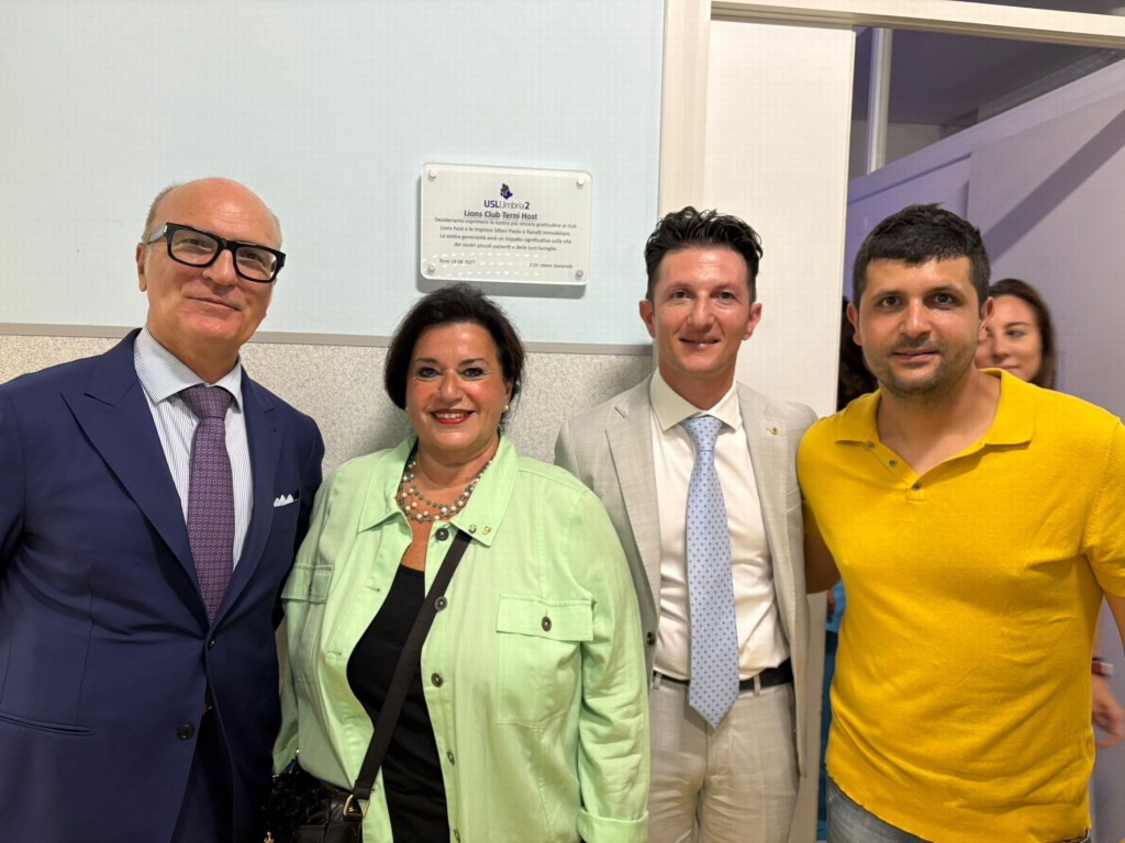 Quattro persone sorridenti in una stanza con una targa sulla parete, durante l'inaugurazione della nuova stanza multisensoriale presso il dipartimento di neuropsichiatria infantile della Usl Umbria 2.