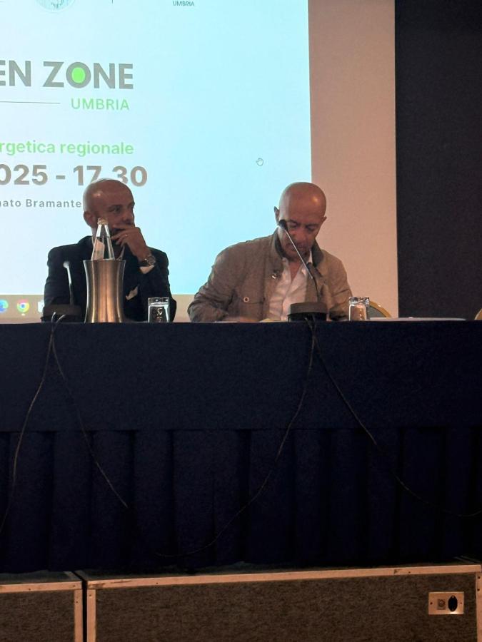 Due relatori siedono a un tavolo durante l'evento 'Green Zone Umbria', con uno schermo dietro di loro che mostra il logo dell'iniziativa e dettagli sull'orario.