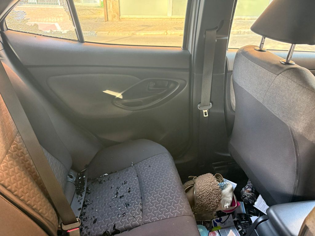 Interior of a car's back seat with glass shards scattered on the floor and a damaged window.