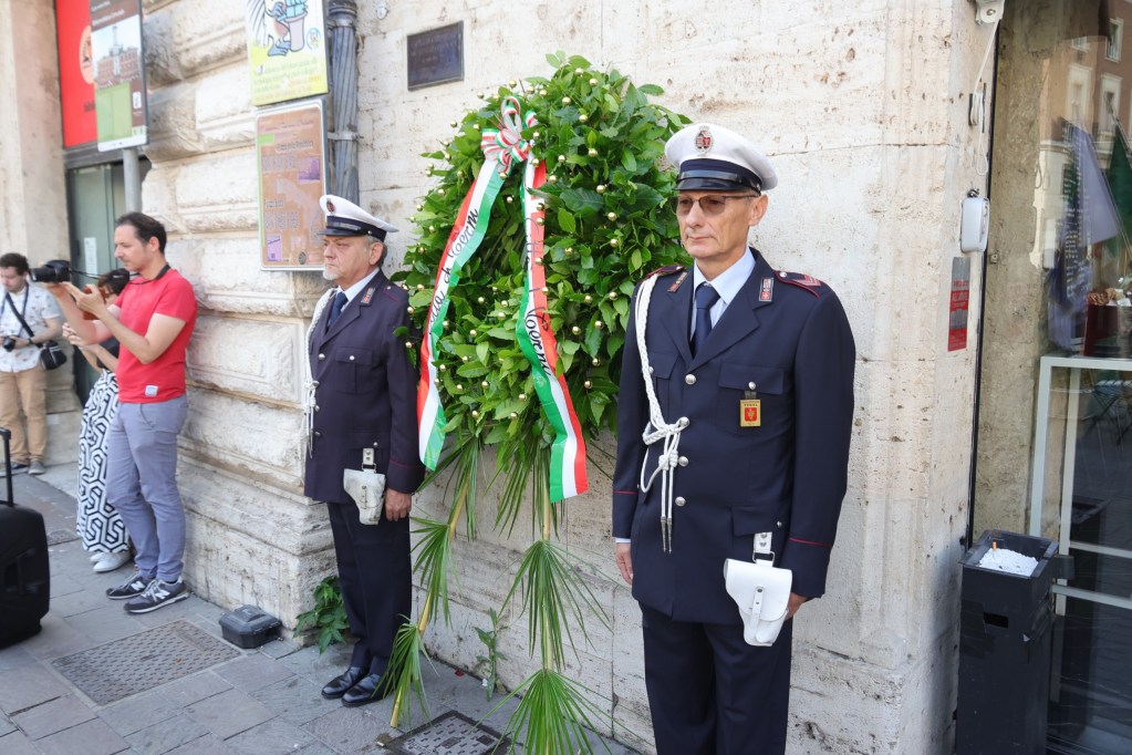 Due membri delle forze dell'ordine in uniforme accanto a una corona d'alloro con nastri tricolori, durante le celebrazioni per l'81° Anniversario della Liberazione della Città di Terni.