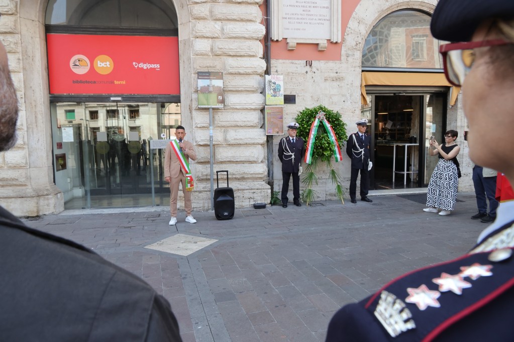 Cerimonia commemorativa per l'81° Anniversario della Liberazione della Città di Terni, con un oratore in piedi davanti alla biblioteca e una corona d'alloro.