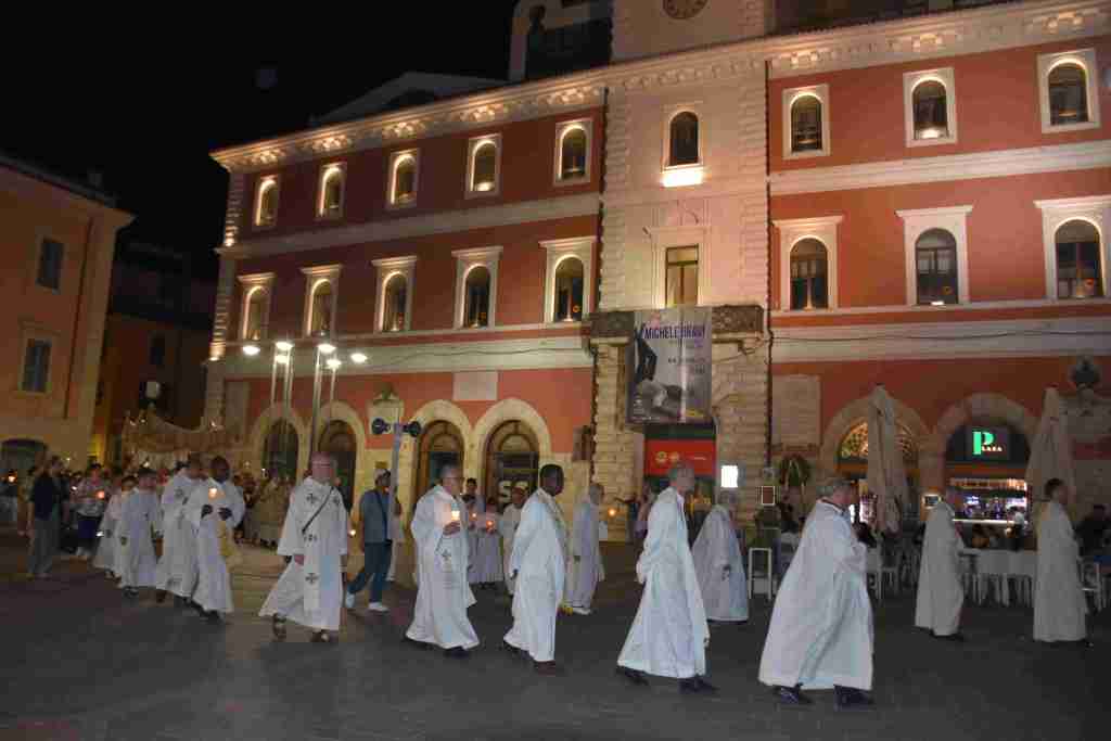 Processione notturna durante la celebrazione della solennità del Corpus Domini a Terni, con partecipanti in abiti religiosi che portano candele.