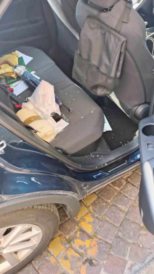 Interno di un'auto danneggiata, con vetri rotti e oggetti sparsi sul sedile. Vi sono attrezzi e sacchetti lasciati all'interno.