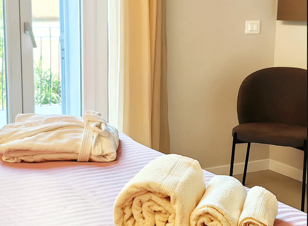 Interno di una suite di lusso, con asciugamani arrotolati su un letto e una sedia in legno visibile sullo sfondo.
