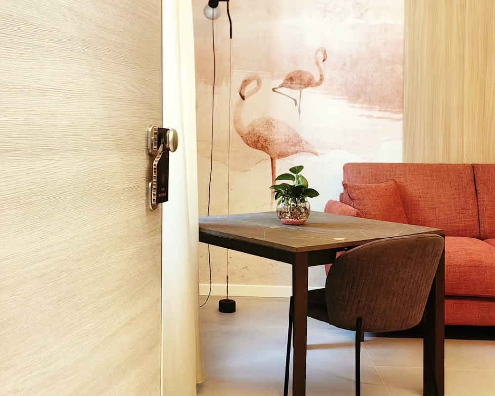 Interno di una suite del Terni Luxury Suite, con un tavolo e una sedia, un divano rosso e un muro decorato con immagini di fenicotteri.