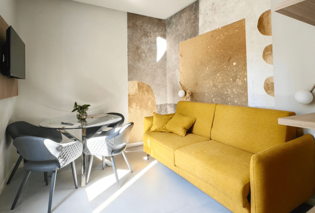 Interno di una suite presso 'Terni Luxury Suite – Tre Monumenti', con un divano giallo e un tavolo di vetro circolare, arredato con stile moderno.