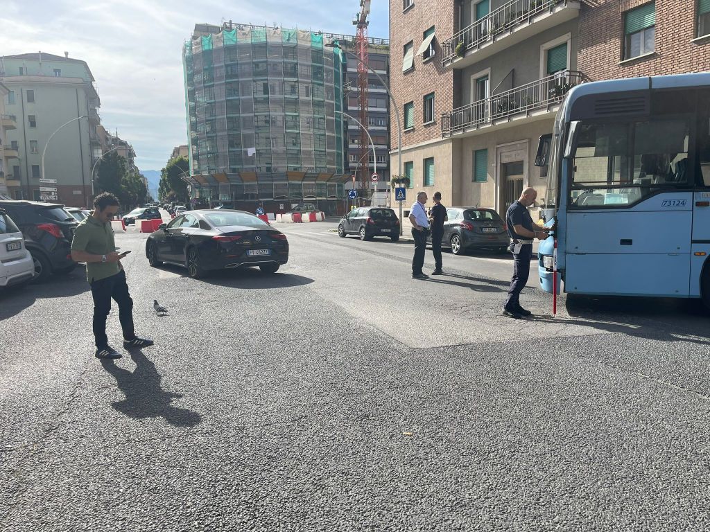 Incidente stradale che coinvolge un autobus e un'autovettura presso l'incrocio tra via Borsi e via Battisti a Terni. Si vedono poliziotti sul posto e un uomo che osserva.