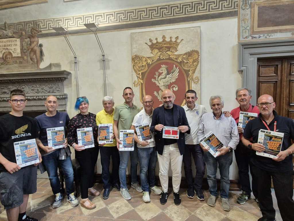 Gruppo di persone in abiti informali che tengono manifesti del Perugia Urban Night Trail, in una sala con decorazioni storiche.
