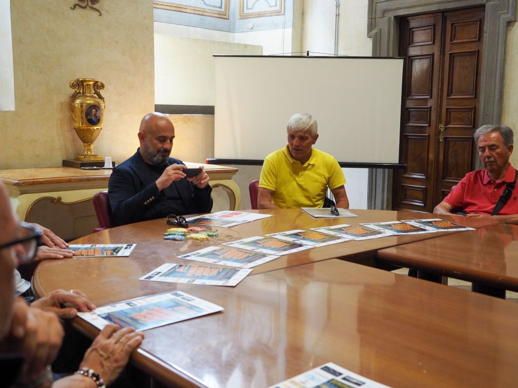 A group of men seated around a wooden table in a formal setting, discussing documents related to the Perugia Urban Night Trail event.