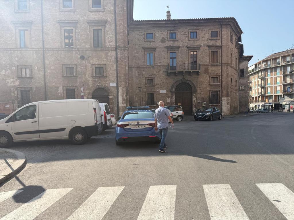 A man walking in a bustling urban area with various parked cars and historic buildings in the background.