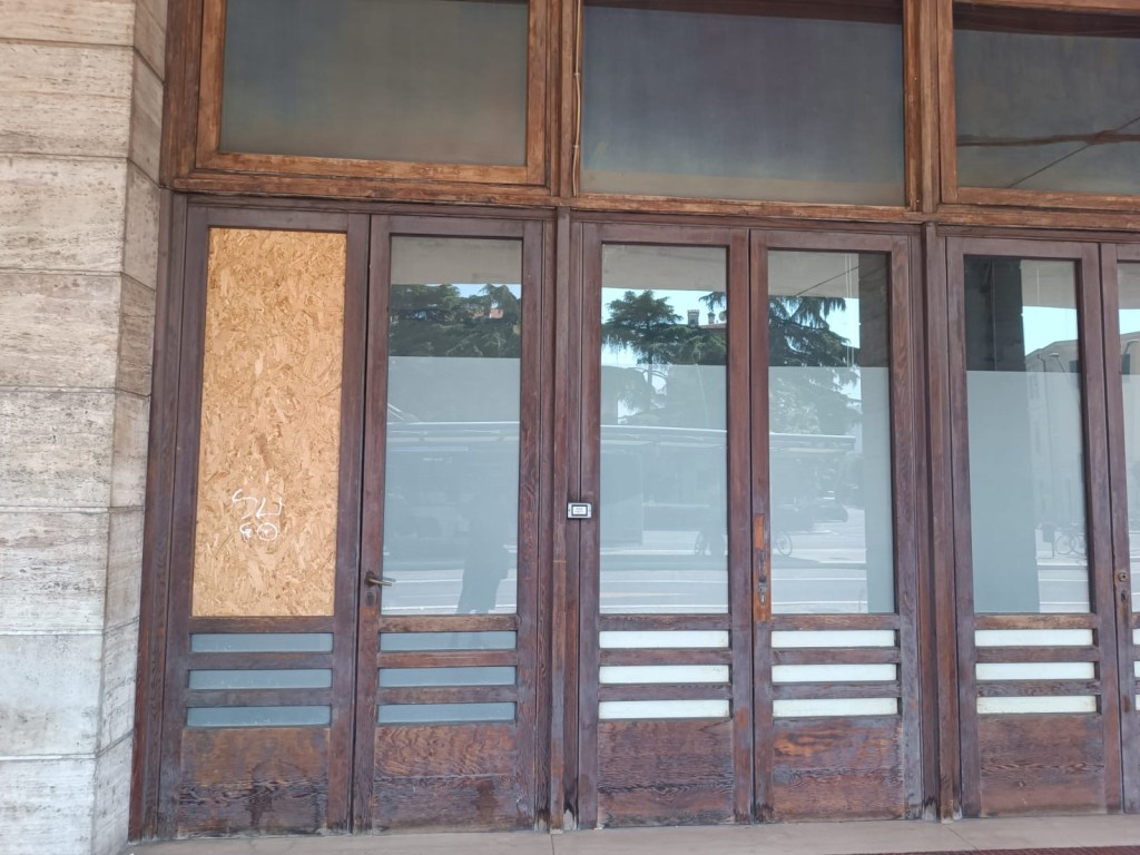 Wooden double doors with a boarded-up section on the left, partially obscured glass panes, and a simple horizontal design.
